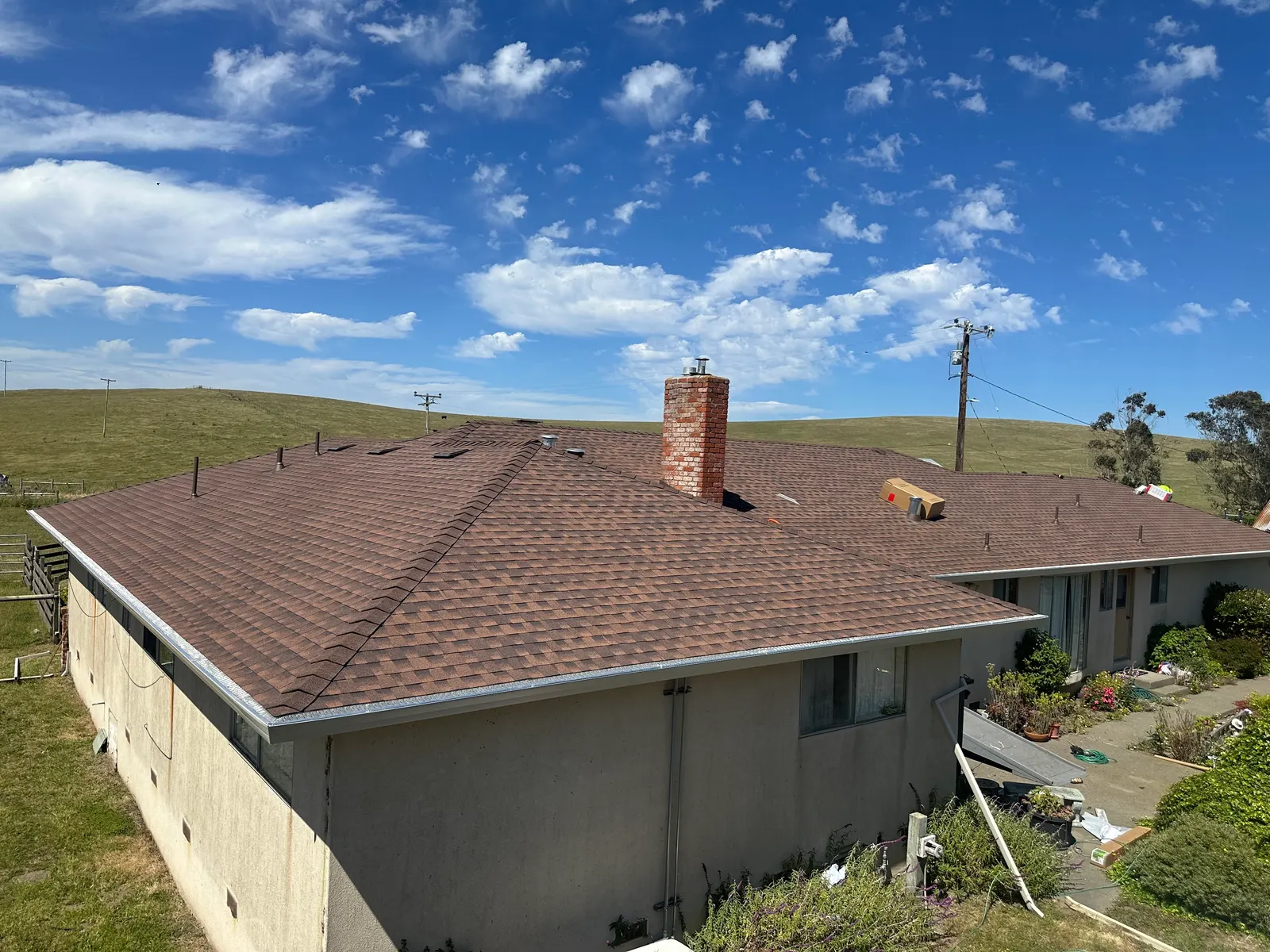 Brown shingle hip roof with brick chimney on a coastal ranch home