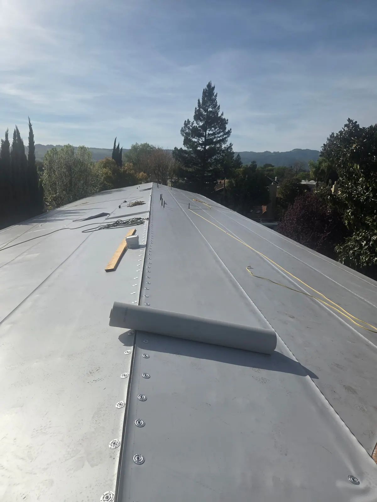 Gray metal panel low-slope roof during installation with underlayment rolls staged