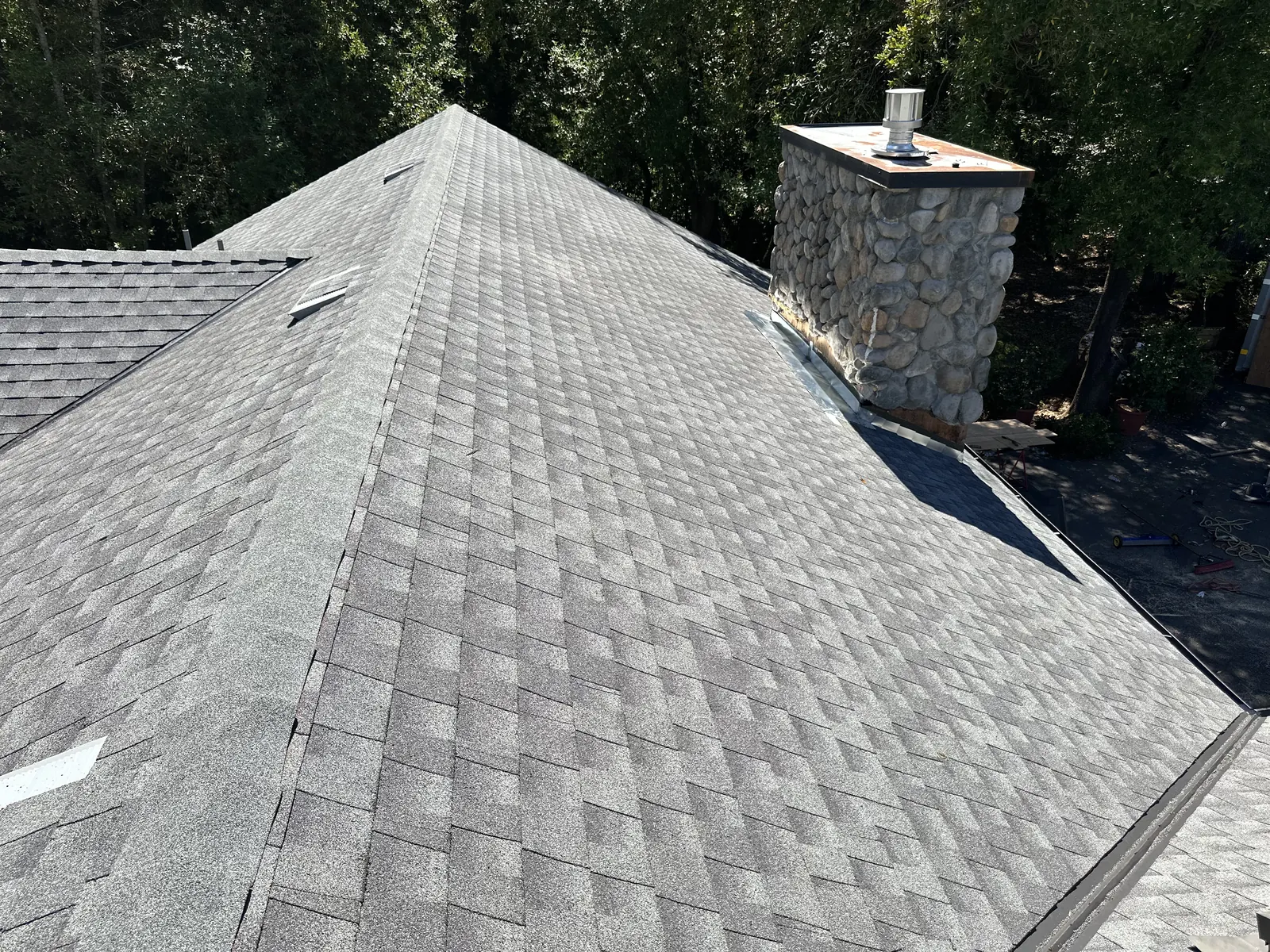 Completed gray architectural shingle roof beside a river-rock stone chimney on a Sonoma home