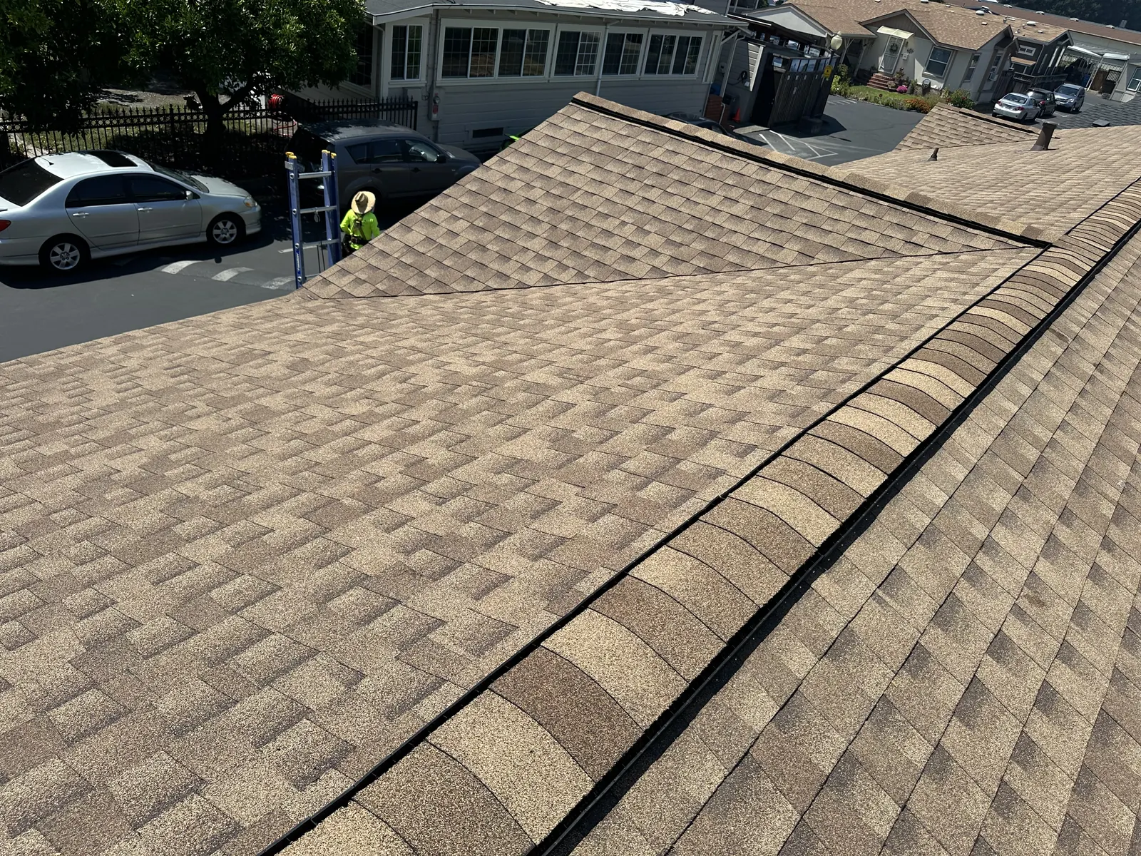 Completed tan architectural shingle roof and ridge cap on a Healdsburg manufactured home, crew at ground level below