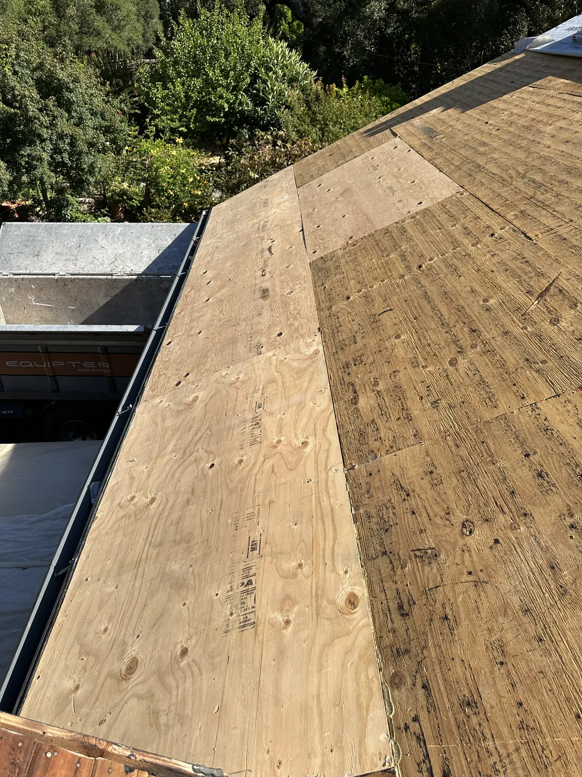 New plywood roof decking on a steep slope during a Sonoma roof replacement, debris trailer staged below at the eave