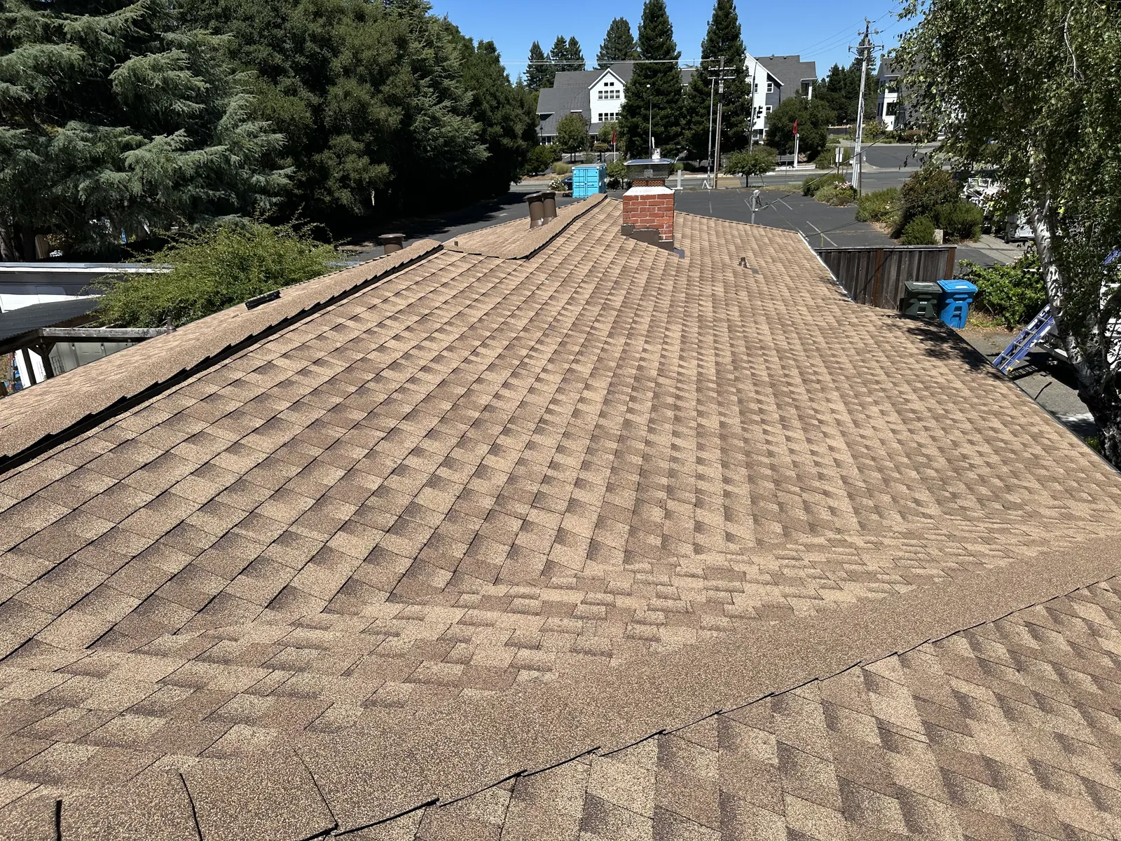 Wide view of a completed tan architectural shingle roof with hips and chimney in Sebastopol
